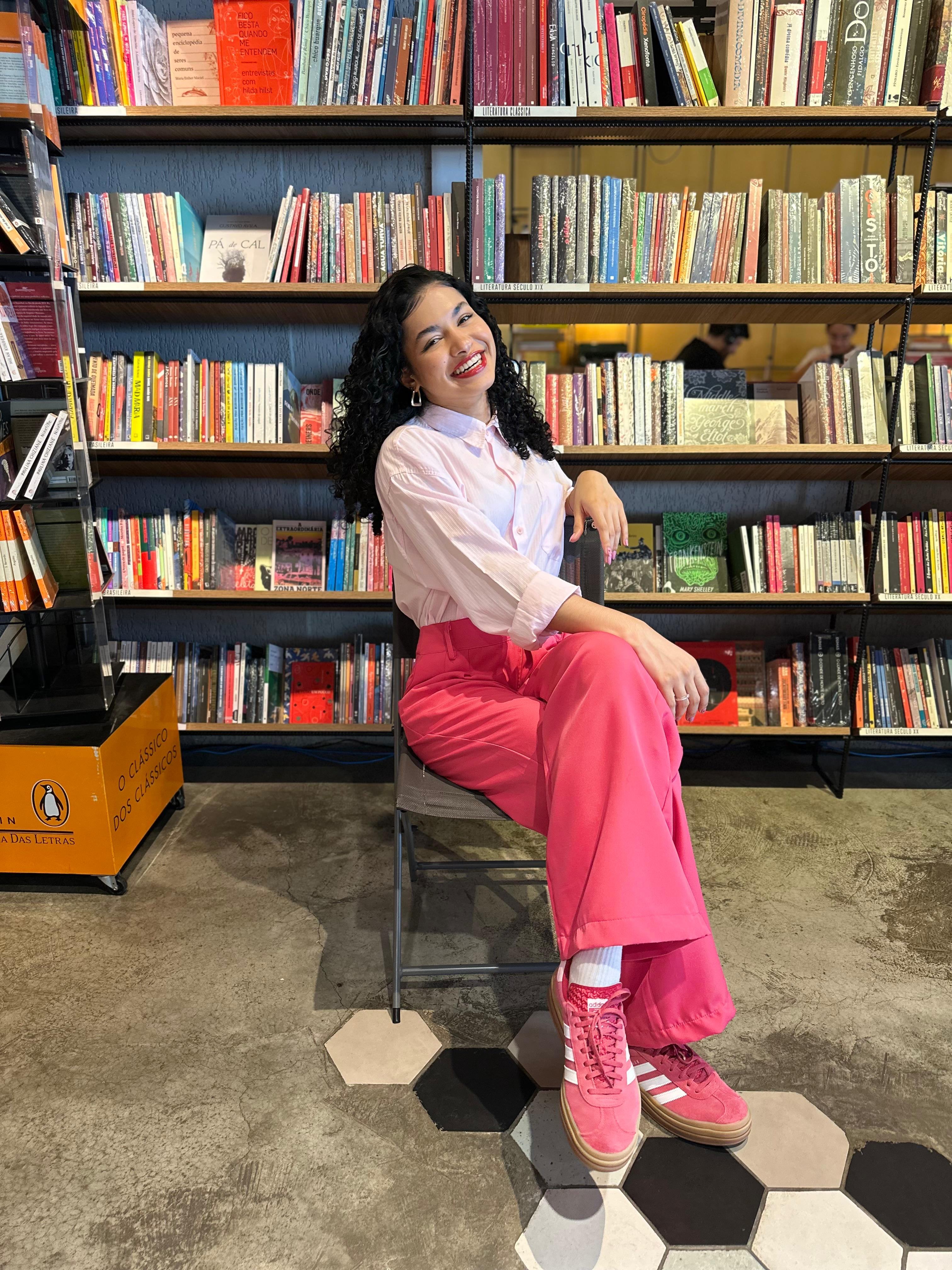 Alana Brígida sentada em uma livraria, em foto usada na seção de palestras.